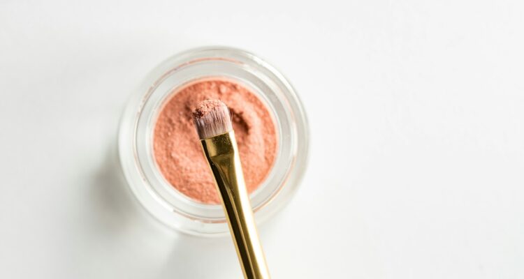 brown makeup brush in front pink powder on glass case